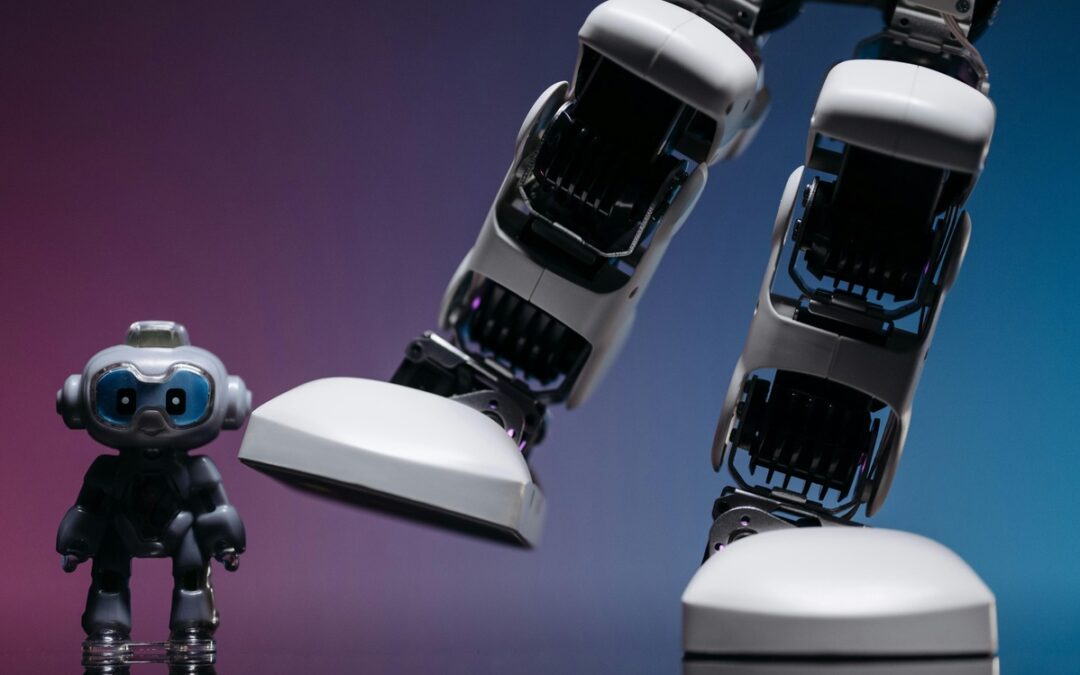 un piccolo robot dalla forma antropomorfa inquadrato per intero, stabile alla base, accanto a un altro robot dalla forma antropomorfa ma molto più grande, di cui si vedono solo gambe e piedi, di cui una gamba è a terra e l'altra è sollevata come in un movimento